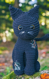 Crochet black cat, sitting upright with pointed ears and a skinny tail. It has shiny plastic eyes and nose, and embroidered whiskers. thumbnail