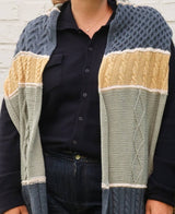 Cropped front view of knit scarf worn draped over shoulders. Each color black section has a different cable motif. thumbnail