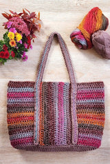 Crochet tote bag laid on pale wooden surface, with two balls of yarn in the upper right corner and a bouquet of fall flowers in the upper left corner. thumbnail