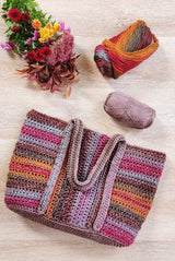 Tote bag with handles laid on top of bag, with yarn balls and flowers in the upper frame. The bag is made in shades of pink, purple, warm yellow, and steely grey blue. The middle panel is striped vertically and the side panels are striped horizontally. thumbnail