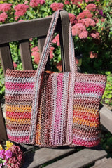 Tote bag sits on wooden chair in backyard, with dark mauve flowers in the background. The bag has shoulder length handles. thumbnail