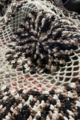 Crochet blanket draped over legs, showing open textures of mesh section in worsted weight yarn. thumbnail