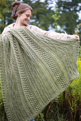 Front view of woman standing with crochet afghan draped over one arm, holding edge out with other hand. thumbnail