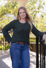 Woman in a long sleeve crochet sweater and jeans stands on a porch. The sweater is a dark green. thumbnail