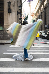Woman holding up colorful blanket while crossing city street thumbnail