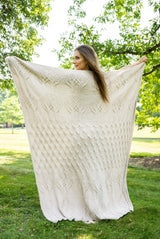 Woman holding up off white tree of life knit blanket showing the full tree design thumbnail