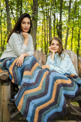 Two women in the woods with a multicolor crochet blanket on their laps. thumbnail