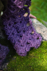 close-up of a violet openwork mesh crocheted scarf draped over a mossy rock outdoor background thumbnail