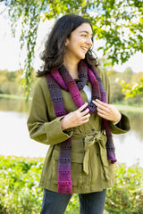 person wearing a multicolored ripple-pattern scarf, olive green jacket, and jeans outdoors near a river thumbnail